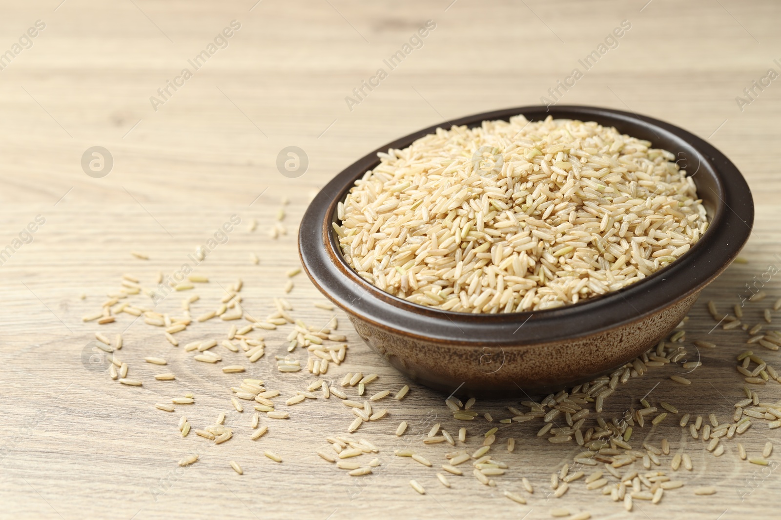 Photo of Brown rice in bowl on wooden table, closeup. Space for text