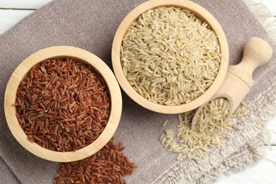 Photo of Different types of brown rice in bowls and scoop on table, flat lay