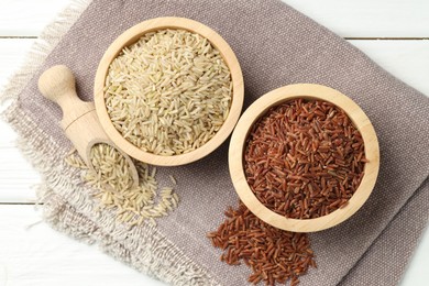 Photo of Different types of brown rice in bowls and scoop on white wooden table, flat lay