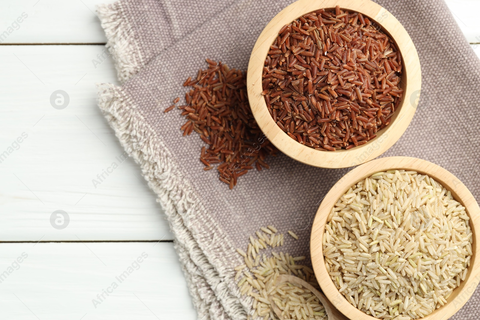 Photo of Different types of brown rice in bowls and scoop on white wooden table, flat lay. Space for text