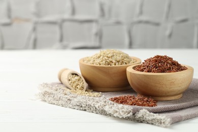 Photo of Different types of brown rice in bowls and scoop on white wooden table, closeup. Space for text