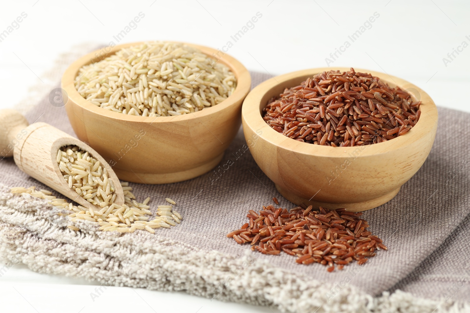 Photo of Different types of brown rice in bowls and scoop on white table, closeup