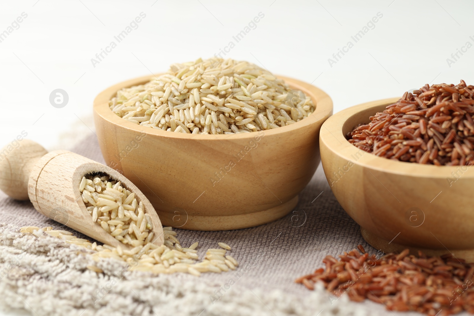 Photo of Different types of brown rice in bowls and scoop on table, closeup