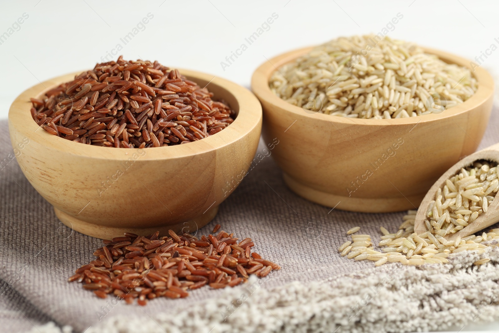 Photo of Different types of brown rice in bowls and scoop on table, closeup