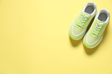 Photo of Sportive shoes. Green sneakers on yellow background, flat lay. Space for text