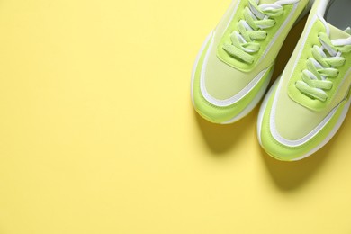 Photo of Sportive shoes. Green sneakers on yellow background, flat lay. Space for text