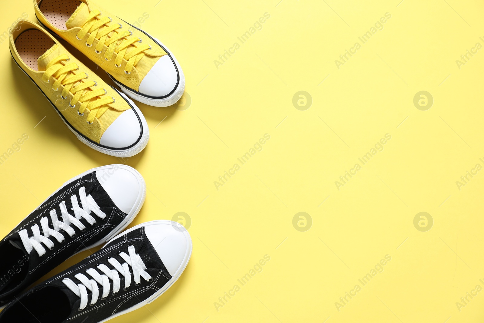 Photo of Sportive shoes. Colorful sneakers on yellow background, flat lay. Space for text