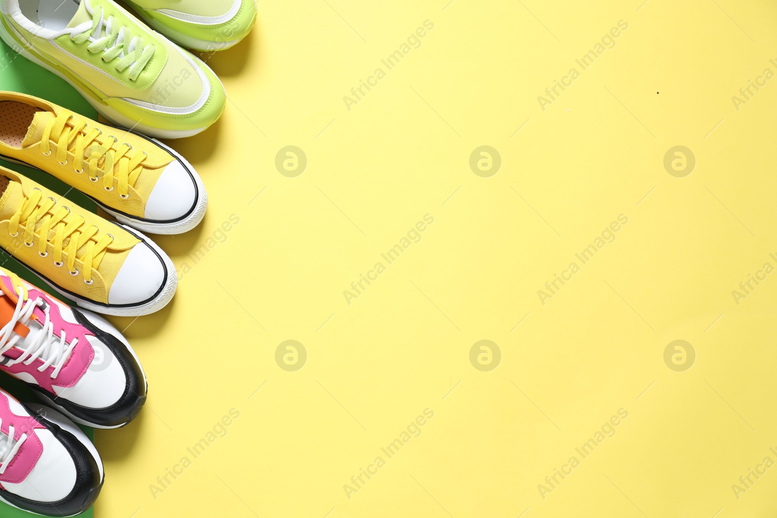 Photo of Sportive shoes. Different sneakers on yellow background, flat lay. Space for text