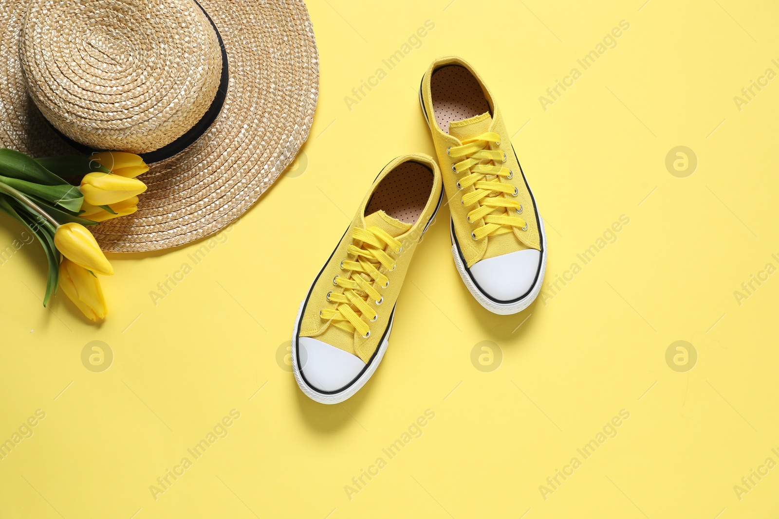 Photo of Stylish shoes, straw hat and tulips on yellow background, flat lay