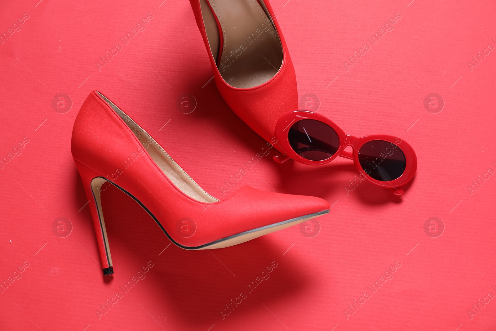 Photo of High heeled shoes and sunglasses on crimson background, flat lay