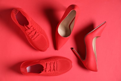 Photo of High heeled shoes and sneakers on crimson background, flat lay