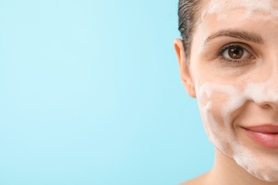 Photo of Attractive woman washing her face with cleansing foam on light blue background, closeup. Space for text