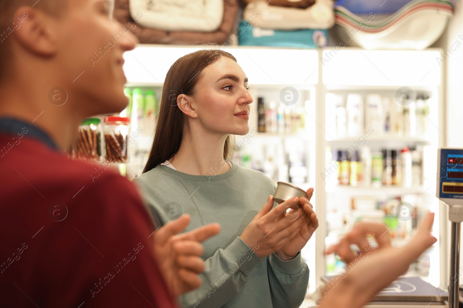 Photo of Pet shop worker helping woman choosing food indoors, selective focus