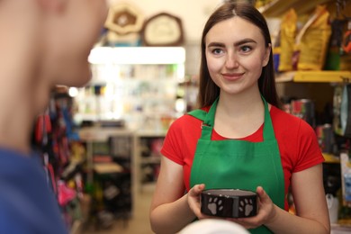 Photo of Pet shop worker helping young man choosing feeding bowl indoors, selective focus