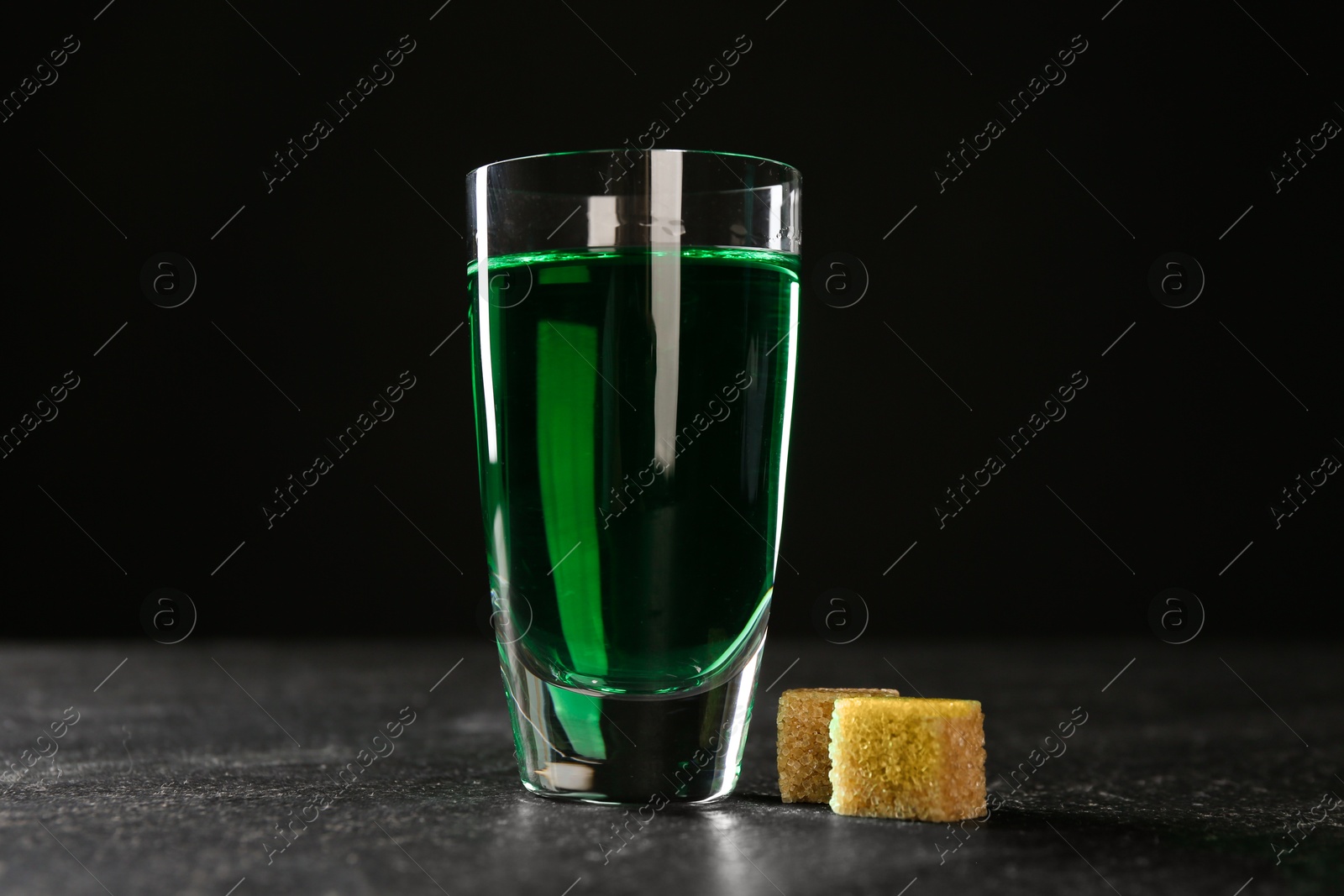 Photo of Absinthe in shot glass and brown sugar on table against black background