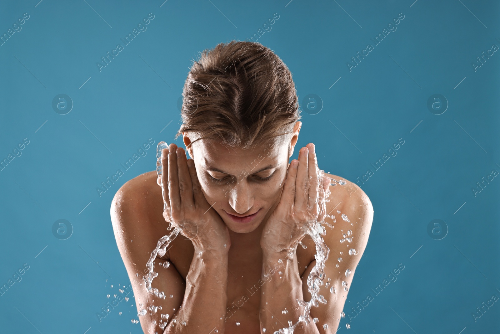 Photo of Handsome man washing his face on blue background