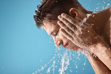 Photo of Handsome man washing his face on blue background. Space for text