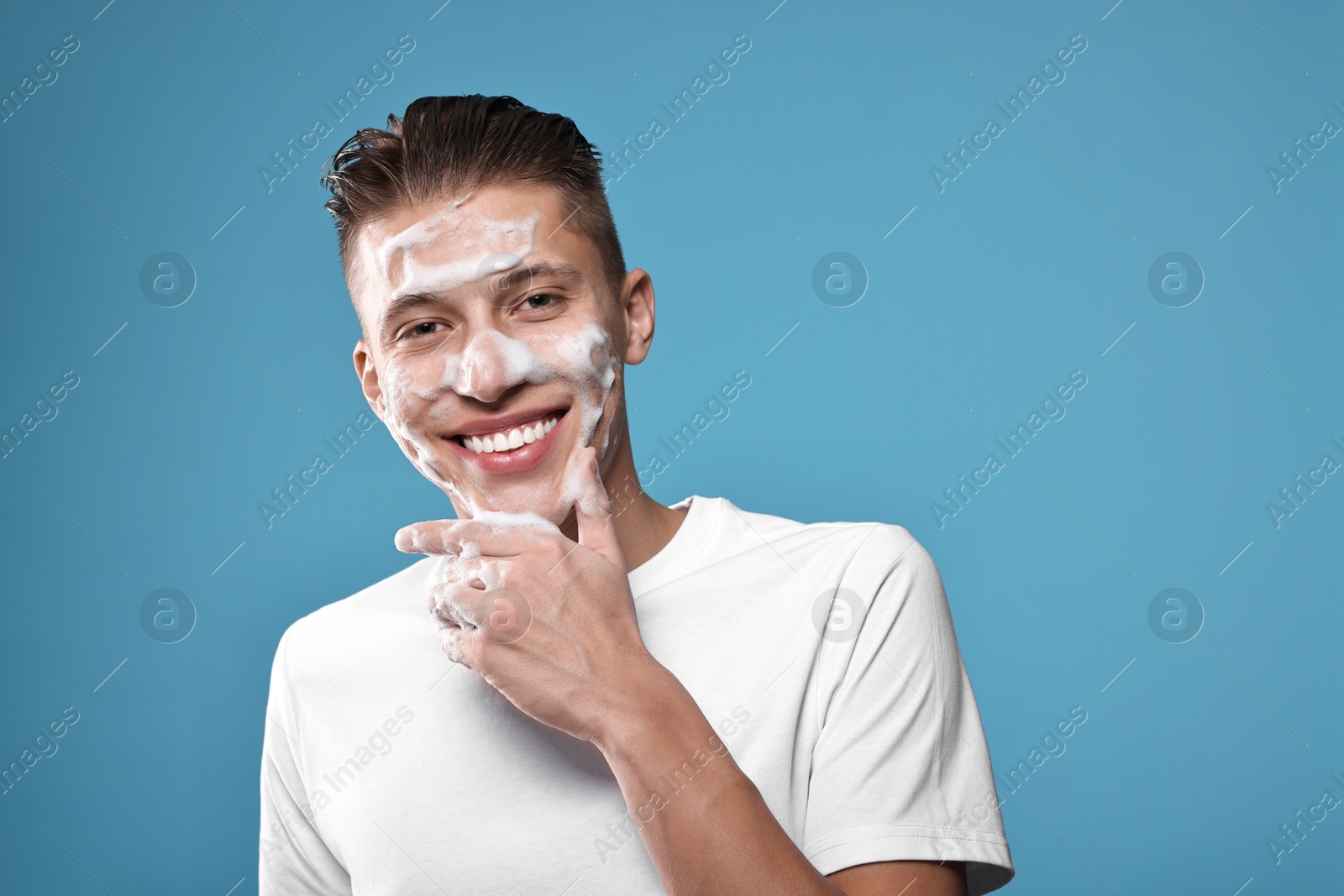 Photo of Smiling man with cleansing foam on his face against blue background. Washing routine