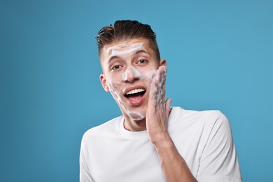 Photo of Surprised man with cleansing foam on his face against blue background. Washing routine