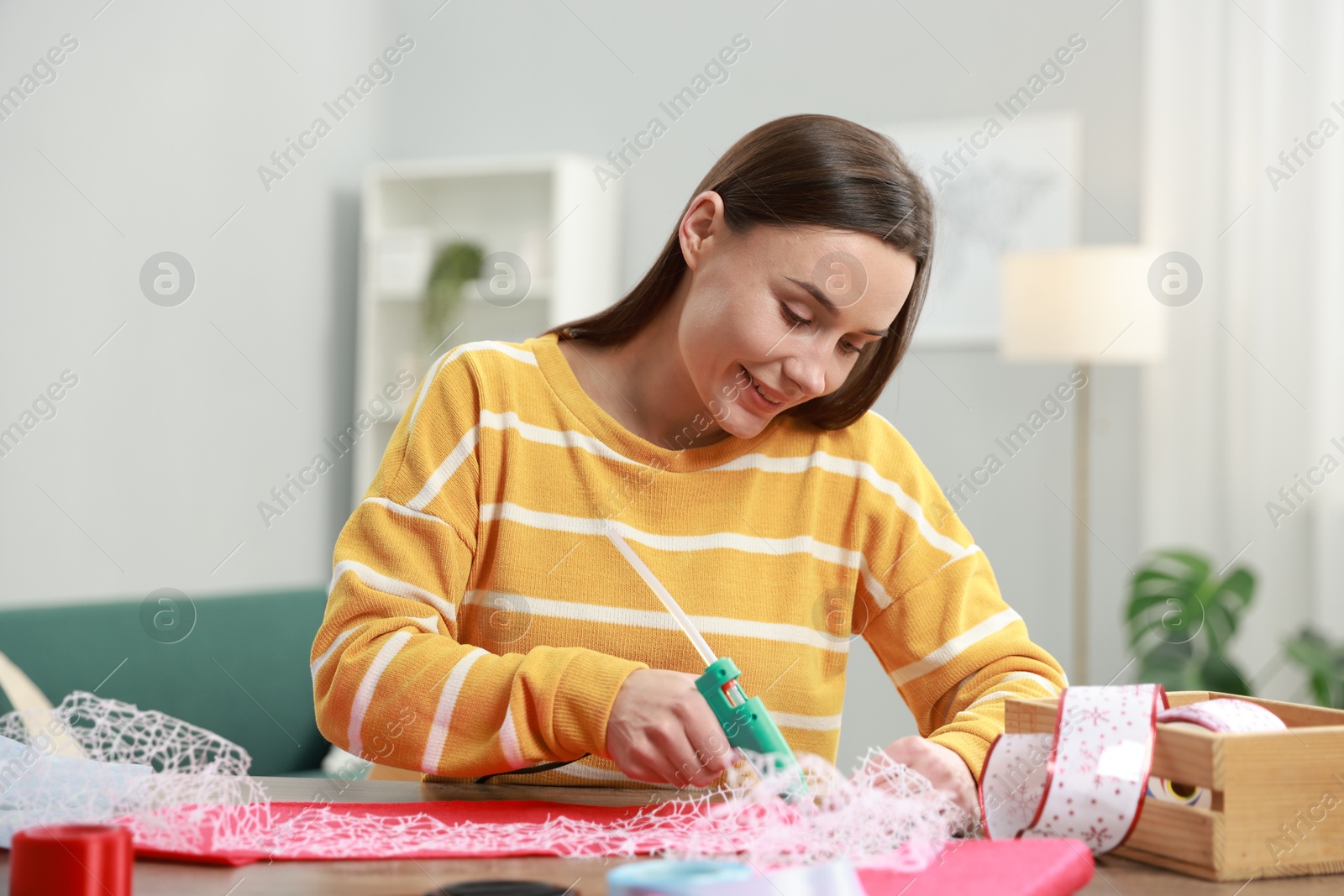 Photo of Woman with hot glue gun making craft at table indoors