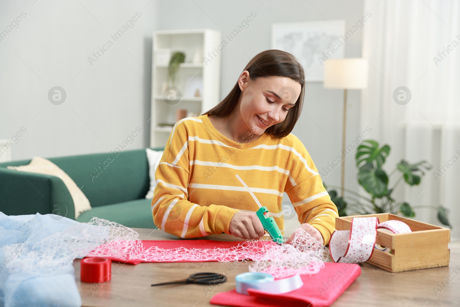 Photo of Woman with hot glue gun making craft at table indoors