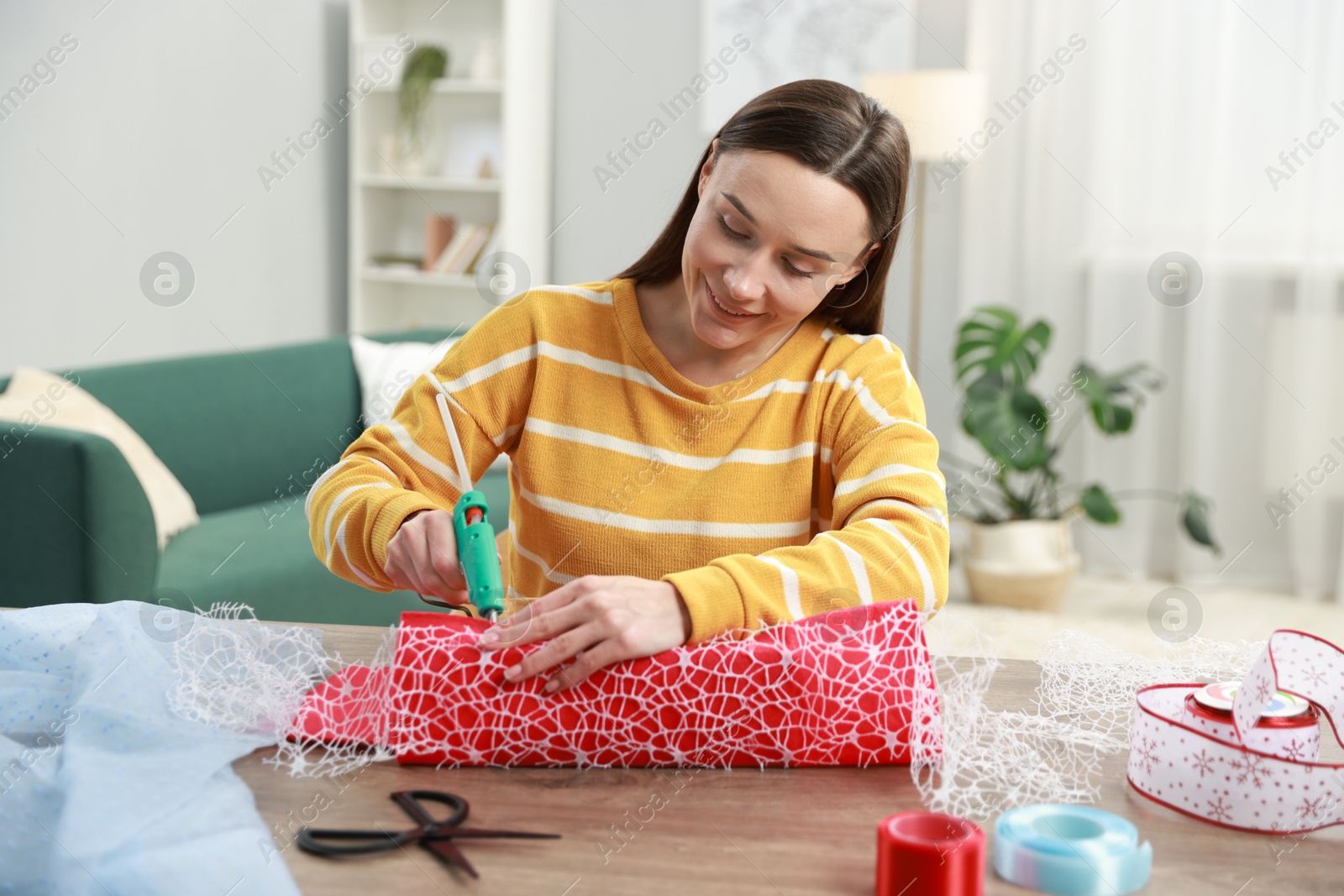 Photo of Woman with hot glue gun making craft at table indoors