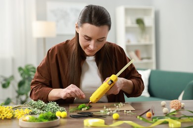 Photo of Woman with hot glue gun making craft at table indoors