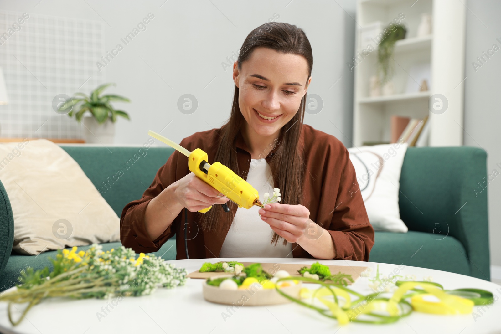 Photo of Woman with hot glue gun making craft at table indoors