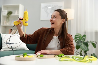 Photo of Woman with hot glue gun making craft at table indoors