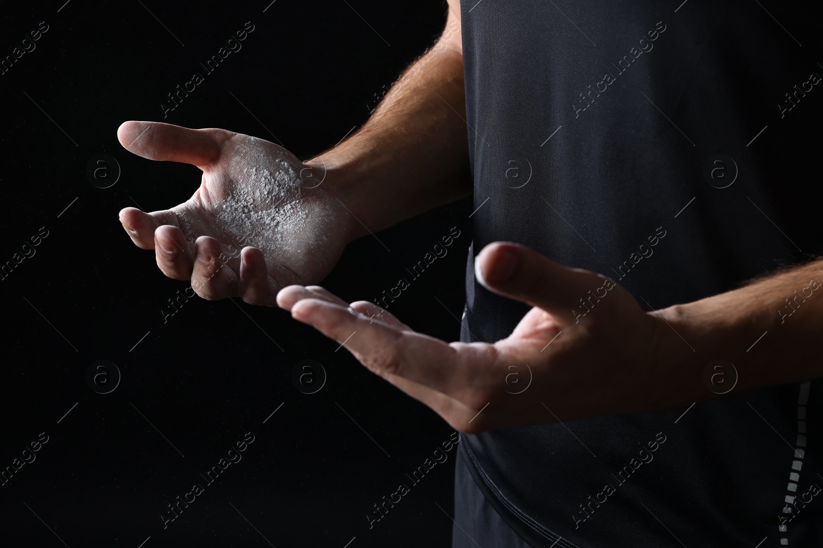 Photo of Man with talcum powder on hands before training against black background, closeup