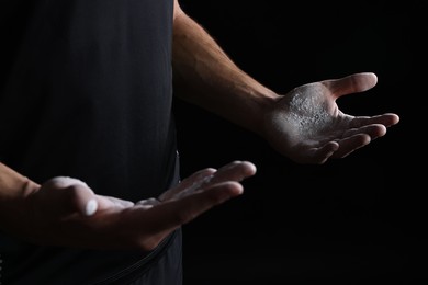 Photo of Man with talcum powder on hands before training against black background, closeup