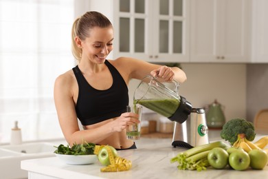 Photo of Weight loss. Woman pouring fresh shake from blender cup into glass at white marble table in kitchen