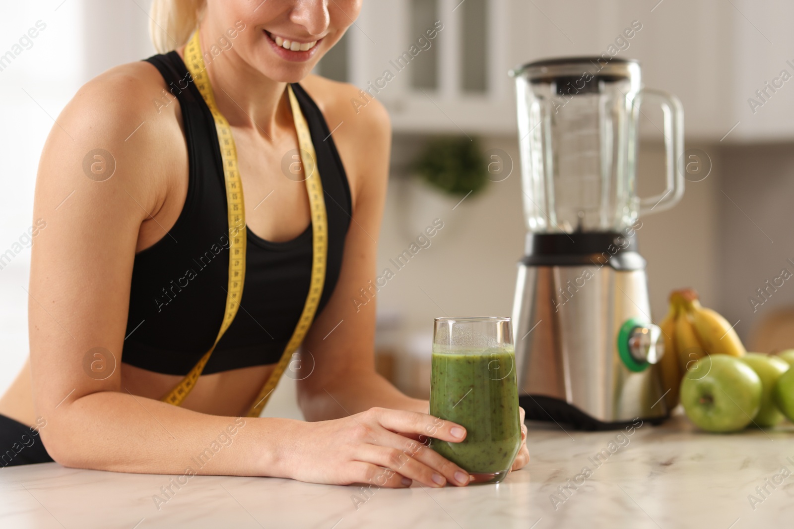 Photo of Weight loss. Woman with glass of healthy shake and measuring tape at white marble table in kitchen, closeup