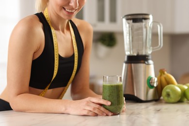 Photo of Weight loss. Woman with glass of healthy shake and measuring tape at white marble table in kitchen, closeup