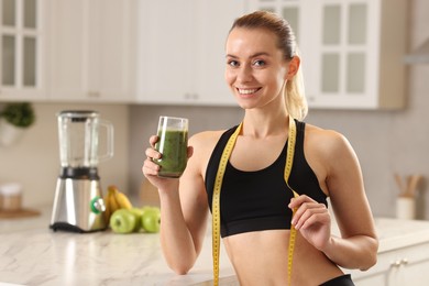 Photo of Weight loss. Woman with glass of healthy shake and measuring tape in kitchen