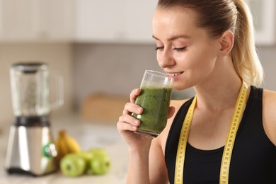 Photo of Weight loss. Woman with measuring tape drinking healthy shake in kitchen, space for text