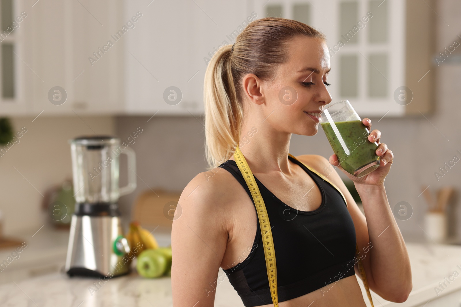 Photo of Weight loss. Woman with measuring tape drinking healthy shake in kitchen, space for text