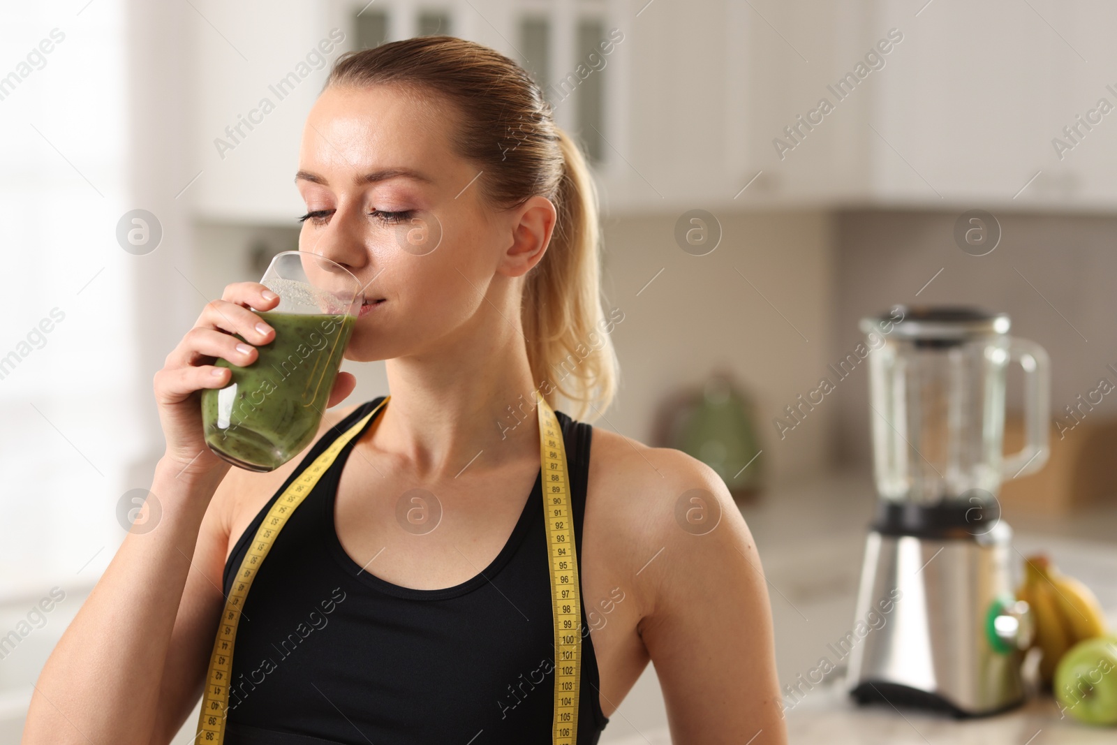 Photo of Weight loss. Woman with measuring tape drinking healthy shake in kitchen, space for text