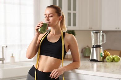 Photo of Weight loss. Woman with measuring tape drinking healthy shake in kitchen