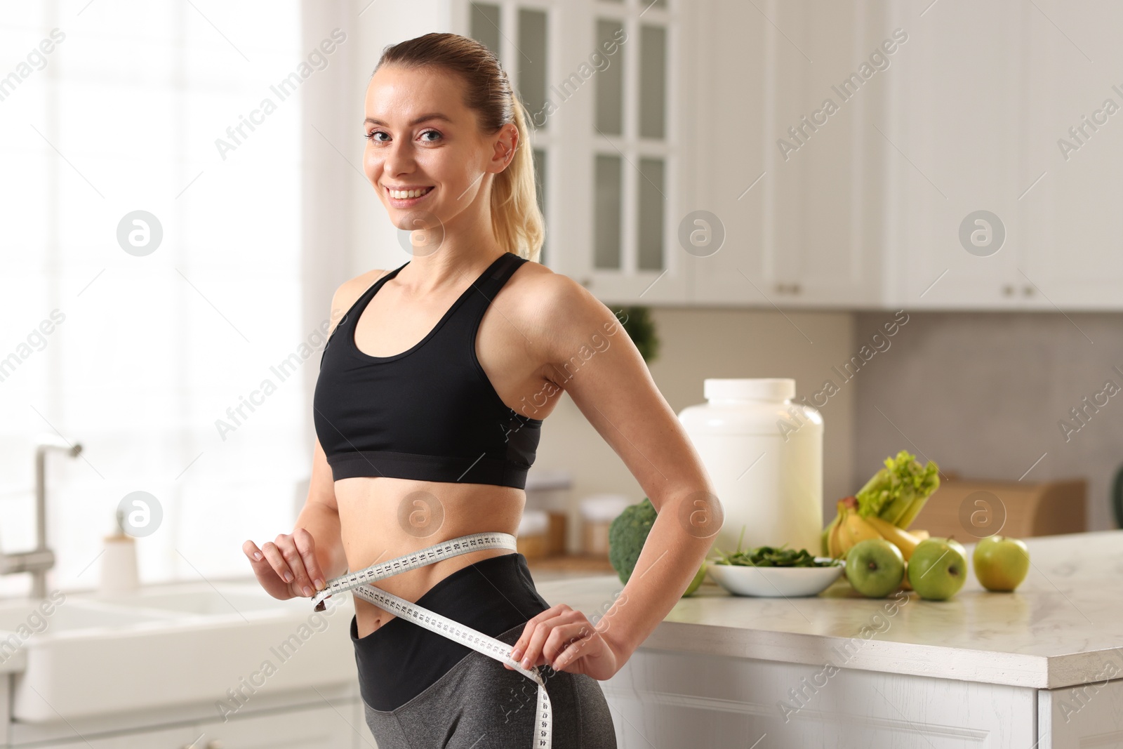 Photo of Weight loss. Woman measuring waist with tape in kitchen