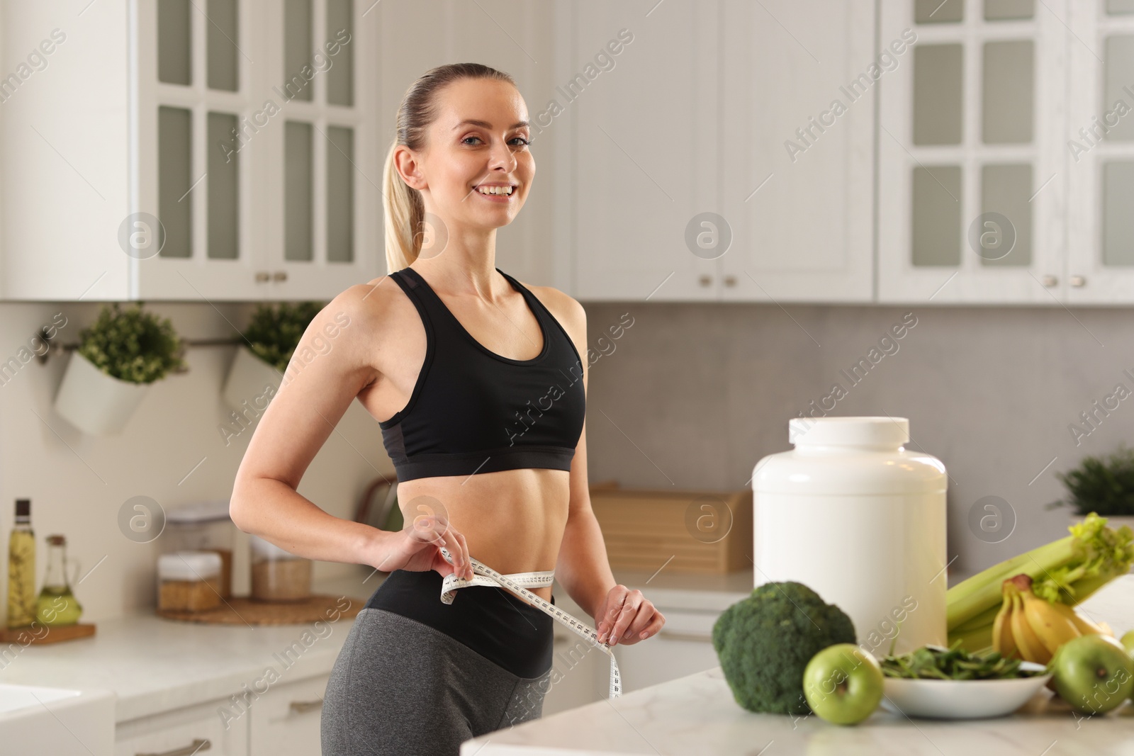 Photo of Weight loss. Woman measuring waist with tape in kitchen