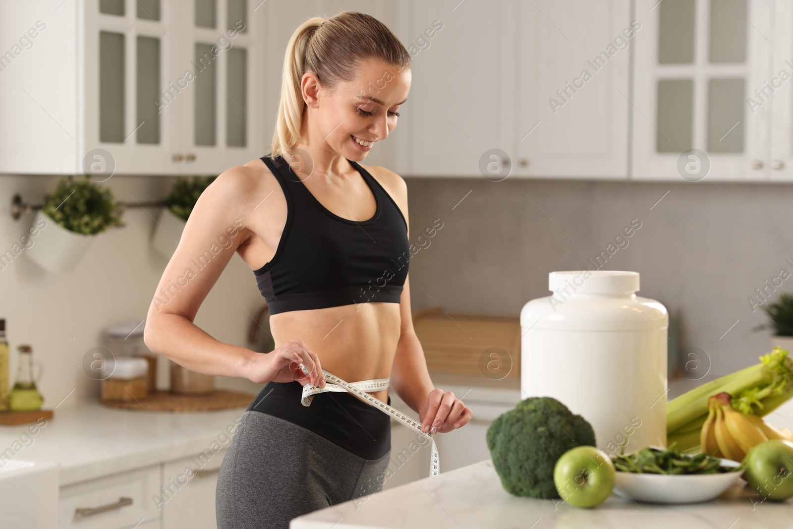 Photo of Weight loss. Woman measuring waist with tape in kitchen