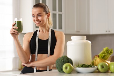 Photo of Weight loss. Happy woman with healthy shake and measuring tape in kitchen