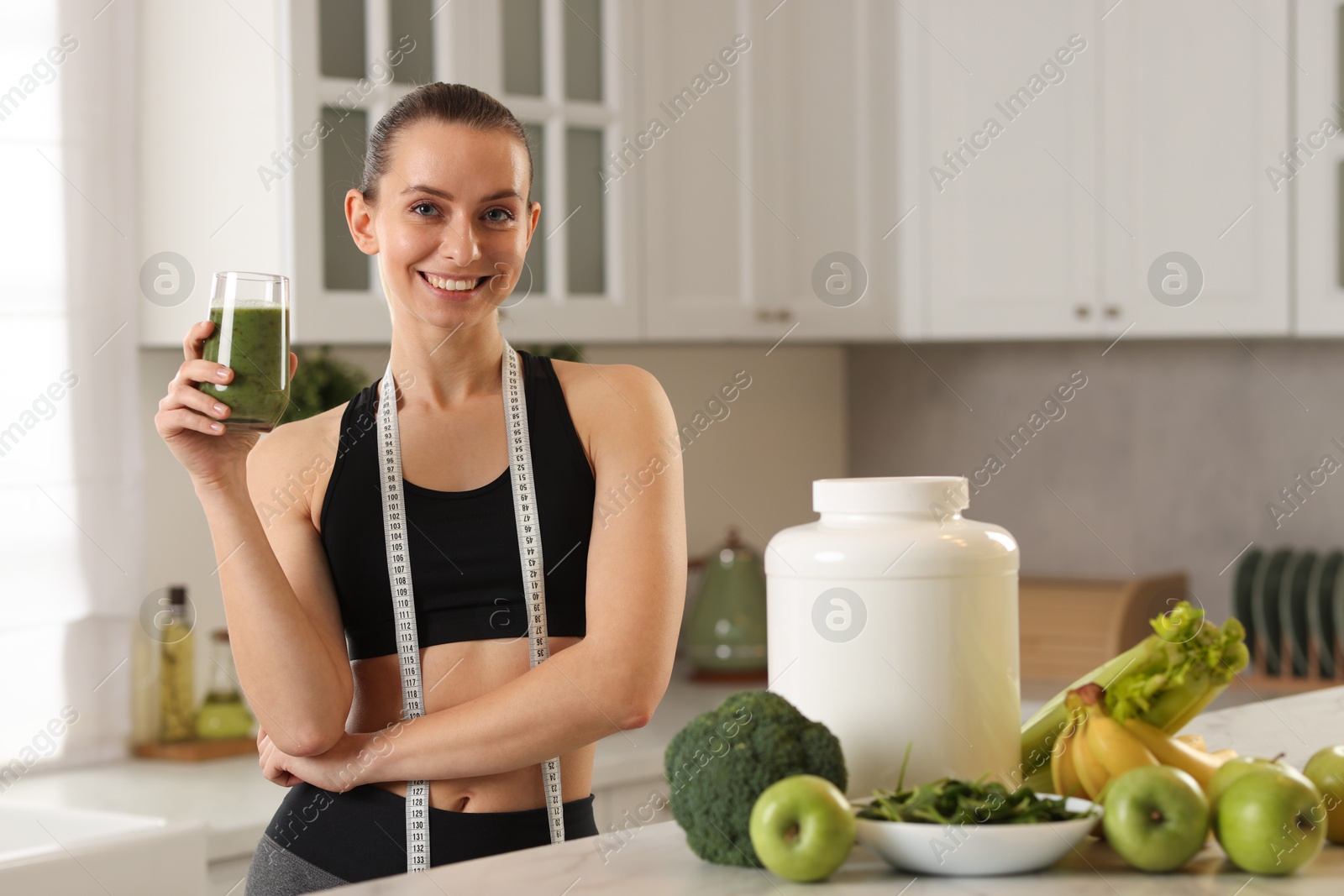 Photo of Weight loss. Happy woman with healthy shake and measuring tape in kitchen