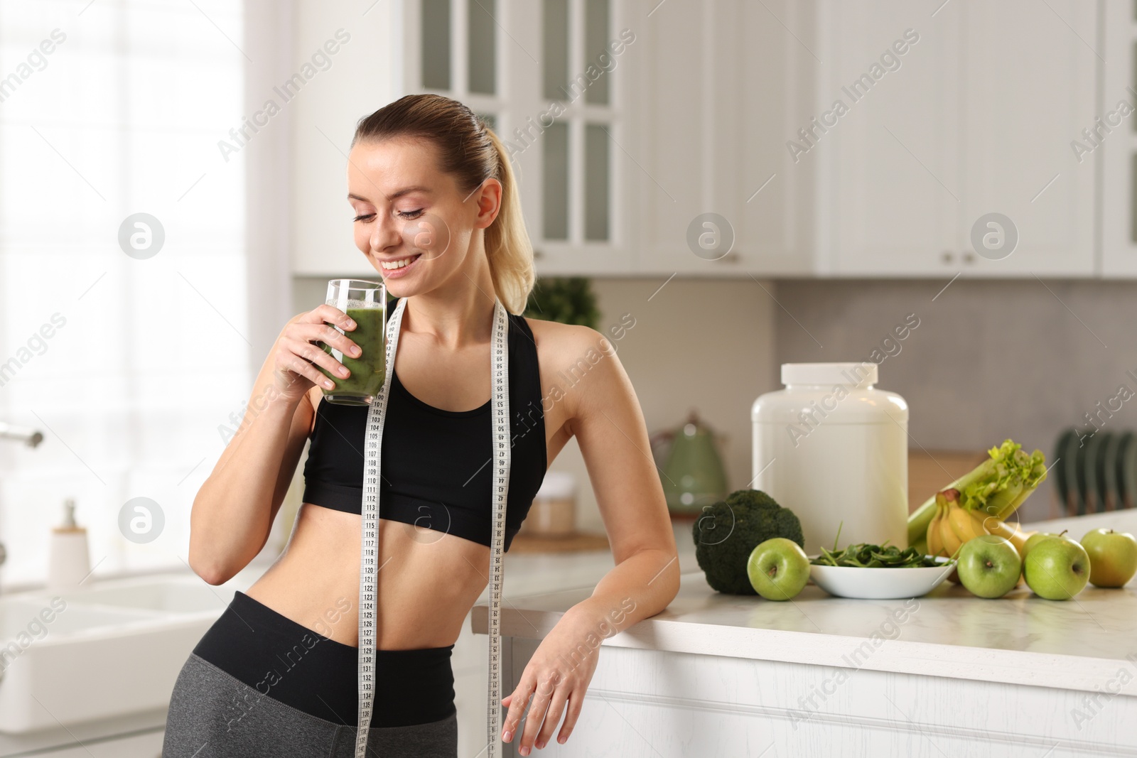 Photo of Weight loss. Happy woman with healthy shake and measuring tape in kitchen