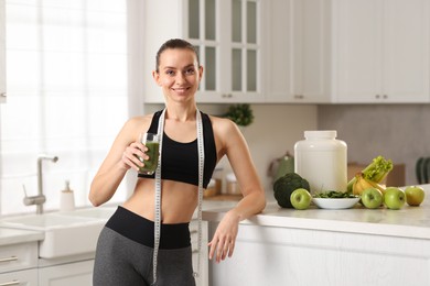 Photo of Weight loss. Happy woman with healthy shake and measuring tape in kitchen