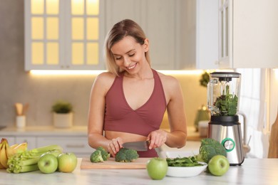 Photo of Weight loss. Happy woman cutting broccoli for healthy shake at table in kitchen