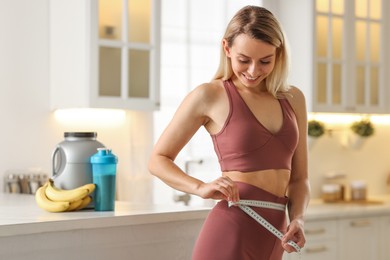 Photo of Weight loss. Woman measuring waist with tape in kitchen