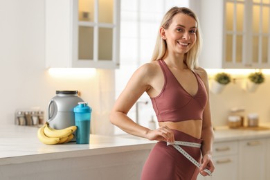 Photo of Weight loss. Woman measuring waist with tape in kitchen