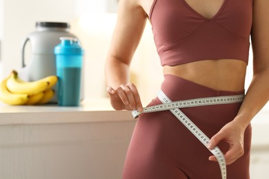 Photo of Weight loss. Woman measuring waist with tape in kitchen, closeup